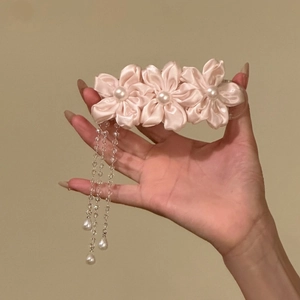 Detailed close-up of a pink satin flower hair clip with elegant dangling pearl tassels