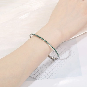 Nahaufnahme eines eleganten Armreifs aus Titanstahl mit grünen Strasssteinen am Handgelenk