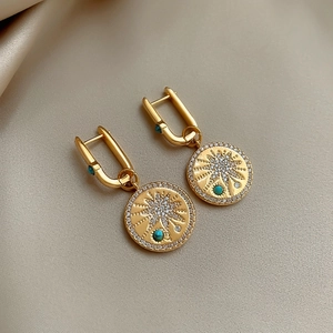 Close-up of 18K gold plated zircon sunburst earrings with turquoise stones on silk background