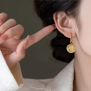 Elegant gold-plated drop earring with sunburst pendant and turquoise detail on model.