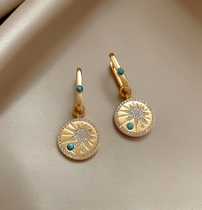 Close-up detail of vintage gold plated starburst pendant earrings with turquoise accents on silk