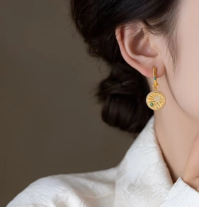 Detailed close-up of a model wearing 18K gold-plated cubic zirconia round pendant earrings.