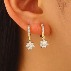 Close-up of gold-plated flower earrings with sparkling zircons on ear.