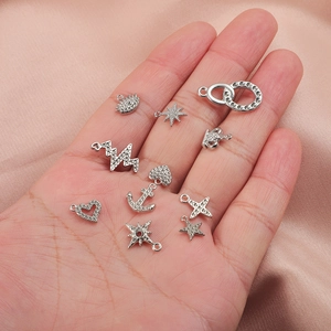 Close-up of silver zircon inlaid charms for necklaces held in a palm on silk background