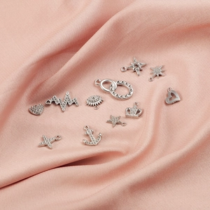 Macro view of various silver cubic zirconia inlaid stainless steel charms on pink satin.