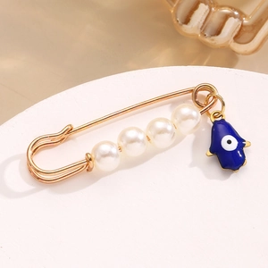Dettaglio di una spilla mano di Fatima dorata con perle e ciondolo occhio blu etnico