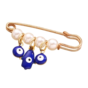 Dettaglio della mano di Fatima dorata e ciondoli occhio blu con perle su spilla elegante