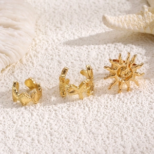 Detailed close-up of gold starfish and sun motif ear cuffs on a beach-themed background