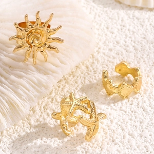Detailed view of gold starfish, sun, and wave ear cuffs on a coral beach background