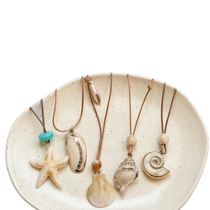 Beach vacation style seashell and starfish necklaces with leather cords on a plate