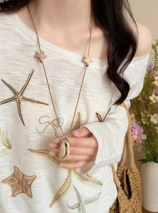 Close-up of a seaside-style seashell pendant necklace with a brown leather cord.