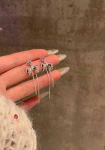 Close-up view of silver bow earrings with sparkling heart zirconia and long tassels held by hand