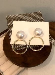 Detalle de pendientes de perlas con aro dorado y diseño de strass brillantes