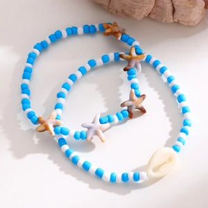 Detalle de conjunto de tobilleras de cuentas azules y blancas con estrella y concha.
