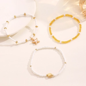 Detalle de conjunto de tobilleras de cuentas con dijes dorados de estrella de mar y concha