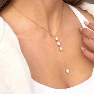 Detailed view of a gold-toned Y-shaped necklace with oval zircon stones on a model.