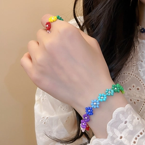 Detail view of a colorful beaded flower bracelet and ring set on a model's hand.