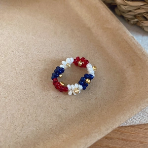 Close-up detail of a handmade red, white, and blue beaded flower ring on a natural background