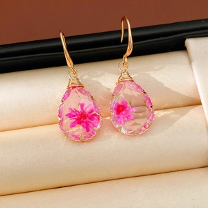 Close-up detail of teardrop resin earrings with pink dried flower and gold hooks