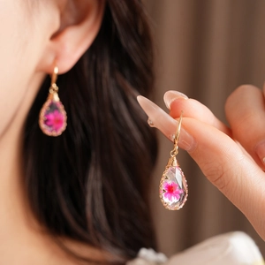 Macro detail of handmade teardrop earrings featuring a real pink resin flower and gold wire