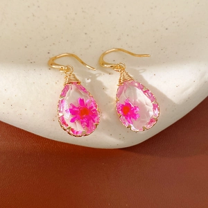 Close-up of handmade resin teardrop earrings featuring a real pink dried flower