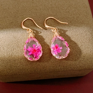 Detailed macro view of gold teardrop resin earrings with embedded pink dried flowers