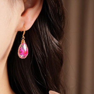 Macro view of teardrop resin earrings featuring pink dried flowers and gold hook.