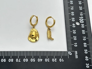 Macro view of asymmetric gold-plated cowboy hat and boot earrings with measuring scale