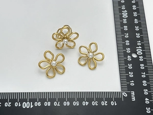 Détail de boucles d'oreilles fleur en or 18 carats avec perles et règle de mesure