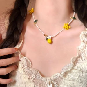 Close-up detail of a sweet vacation style lemon and floral beaded necklace on lace clothing