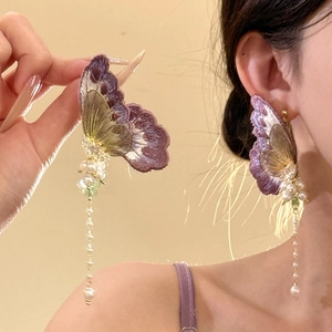 Vue détaillée de boucles d'oreilles papillon brodées à la main avec de longs glands en perles.