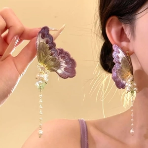 Détail de boucles d'oreilles papillon brodées violettes avec d'élégants glands en perles