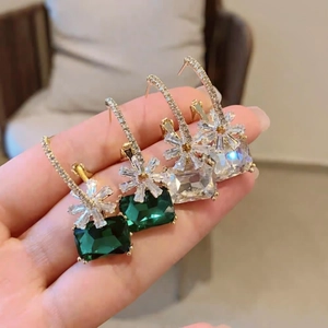 Close-up of elegant flower zircon earrings in emerald green and clear crystal for women