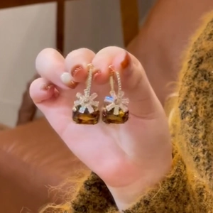 Close-up detail of brown cubic zirconia flower earrings held by a hand showing the design