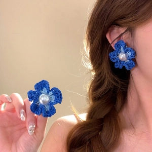 Primo piano di orecchini a fiore intrecciati blu fatti a mano indossati dalla modella