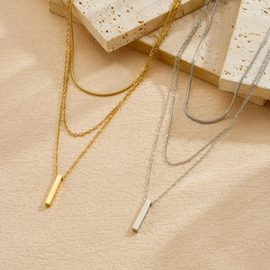 Detailed macro view of gold and silver multi-layer necklaces featuring vertical bar pendants