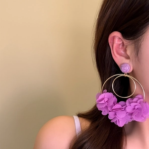 Detail view of oversized purple fabric flower hoop earrings on an East Asian model