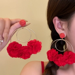 Close-up of large red fabric flower hoop earrings on a model and handheld.