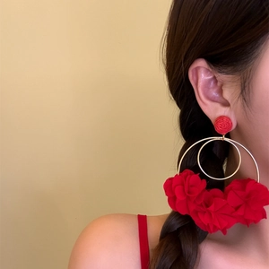 Close-up of oversized red floral hoop earrings worn by a model for a beach vacation look.