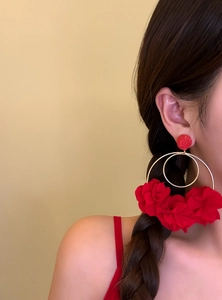 Close-up shot of large red floral hoop earrings worn by a model for beach vacation style.
