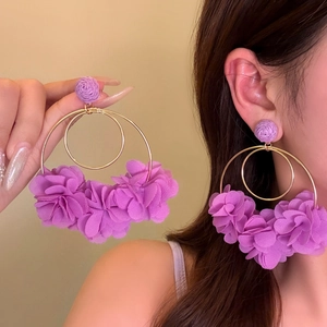 Detailed close-up shot of oversized purple fabric floral hoop earrings worn by a model.