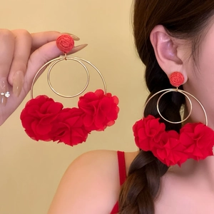 Detailed view of oversized red fabric flower hoop earrings worn by model for beach vacation