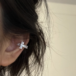 Close-up of sparkling cubic zirconia cross ear cuff on ear without piercing