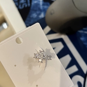 Detailed view of a sparkling zircon cross-shaped ear cuff on a white display card