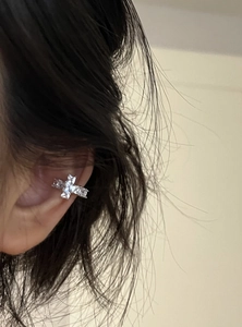 Close-up of a sparkling cubic zirconia cross ear cuff worn on the ear cartilage.