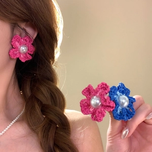 Dettaglio di orecchini a fiore intrecciati a mano rosa e blu con centri in perla eleganti