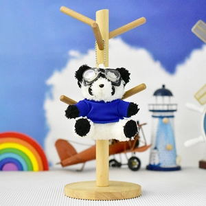 Close-up of a panda plush keychain wearing blue shirt and flight goggles on a wooden stand