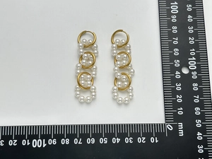 Macro detail of gold layered hoop earrings with white pearls next to a size ruler