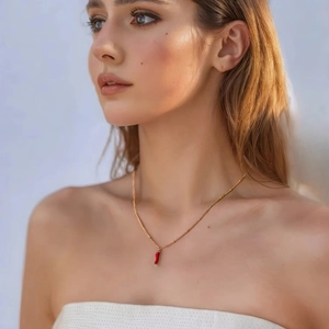 Detail of a gold-plated necklace featuring a vibrant red chili pepper enamel pendant on a model
