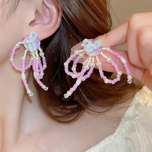 Detailed view of pink beaded flower tassel earrings worn on ear and held by hand